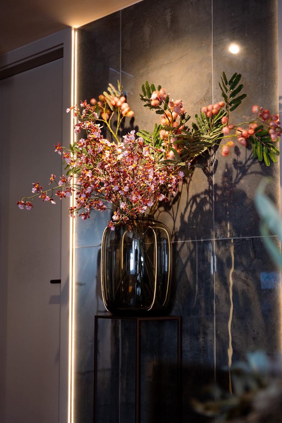 Blumenvase auf einem Podest vor einer dunklen Steinwand